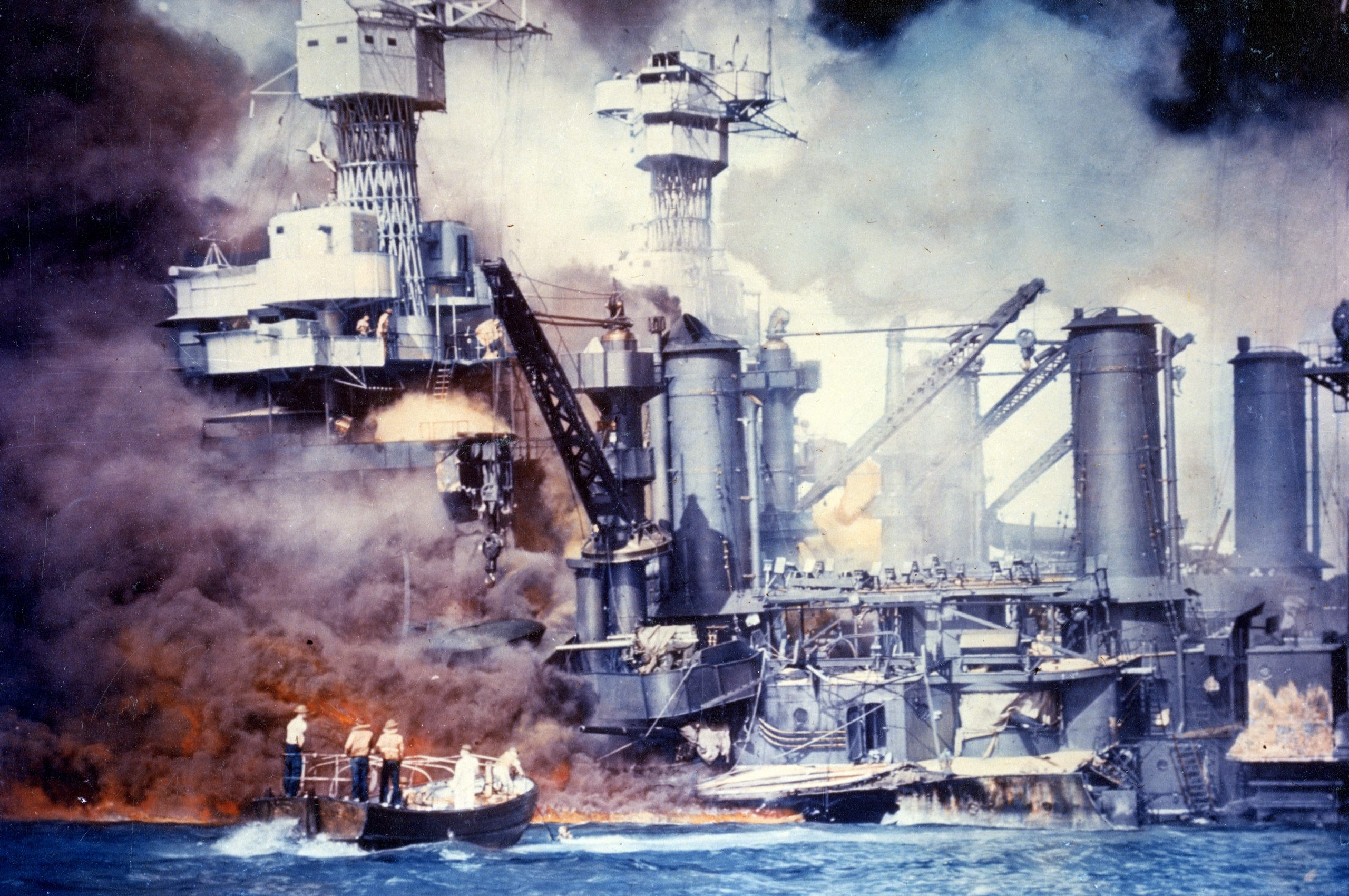 Sailors in a motor launch rescue a survivor from the water alongside the sunken USS West Virginia (BB-48) during or shortly after the Japanese air raid on Pearl Harbor. USS Tennessee (BB-43) is inboard of the sunken battleship.